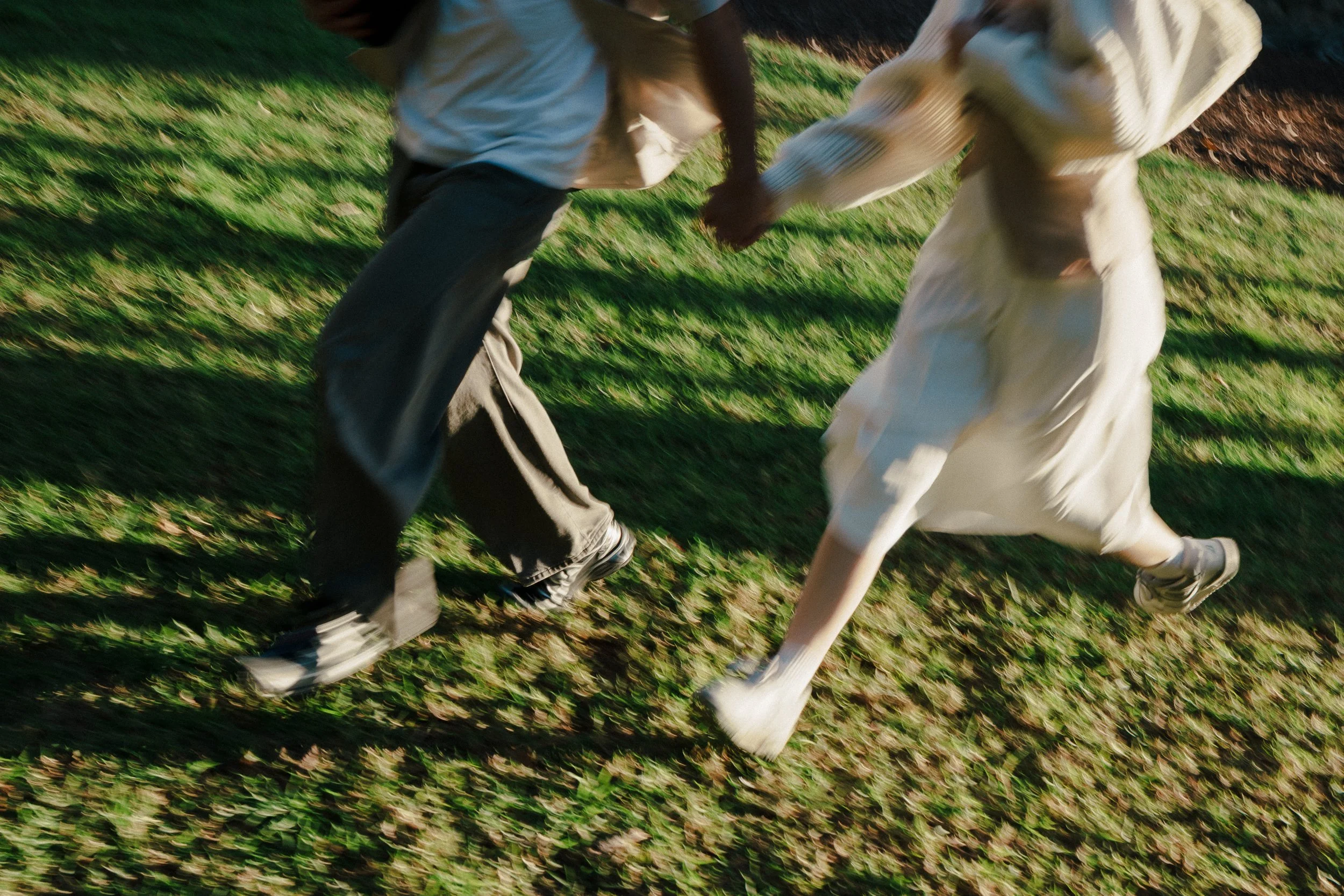 Two children holding hands and running on a grassy field.