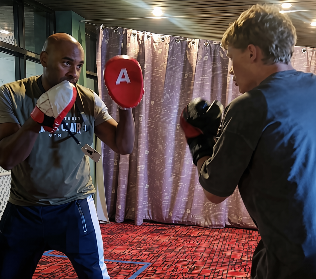 Two men practicing boxing in a gym, wearing boxing gloves and facing each other in a sparring session.