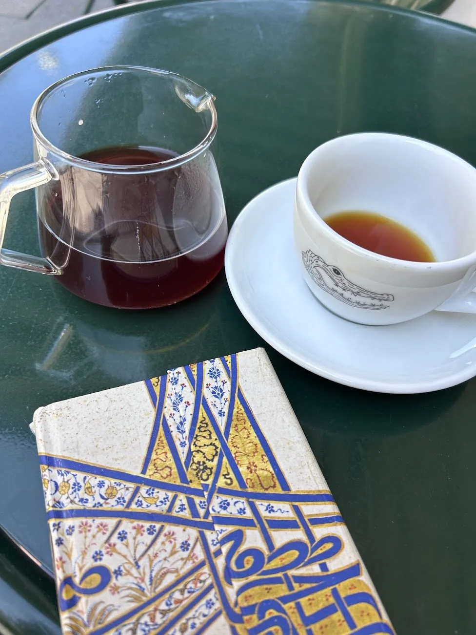 Théière en verre, tasse de thé et carnet aux motifs ottomans sur une table de café.