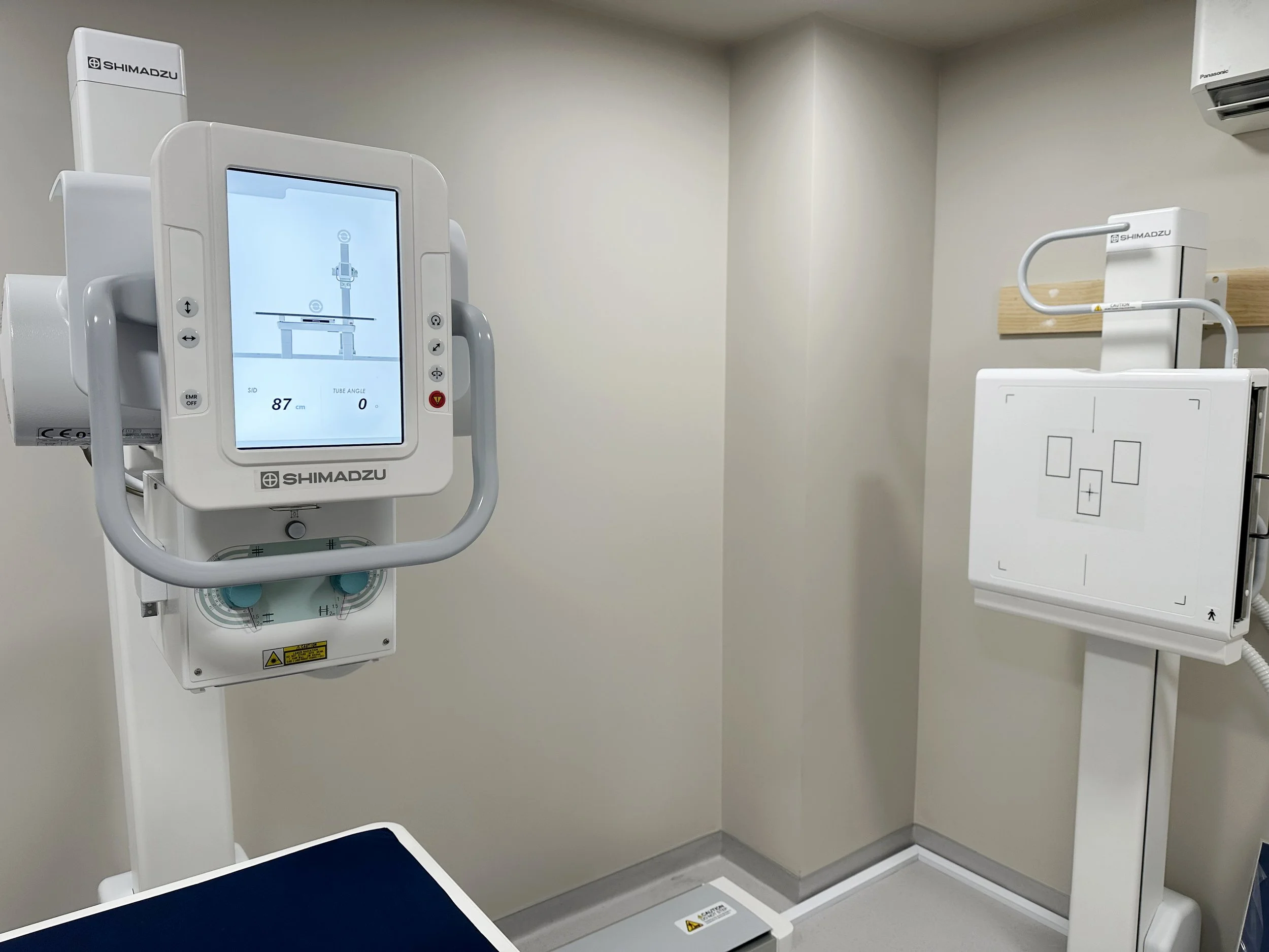 Medical X-ray machine in a hospital room with a display screen and attached parts for imaging.
