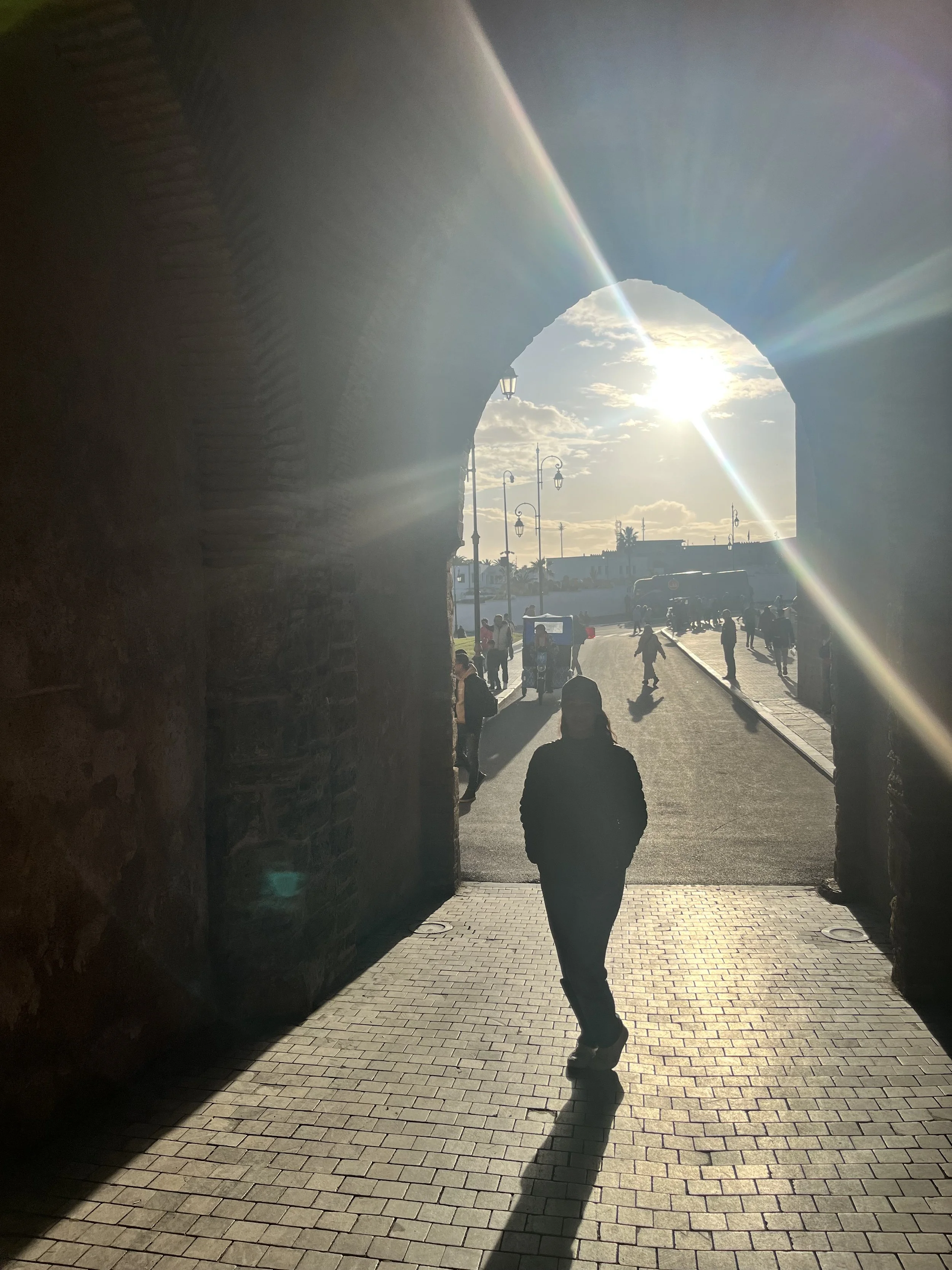 Person walking out of a dark tunnel into bright sunlight, with a city street and people visible in the background.