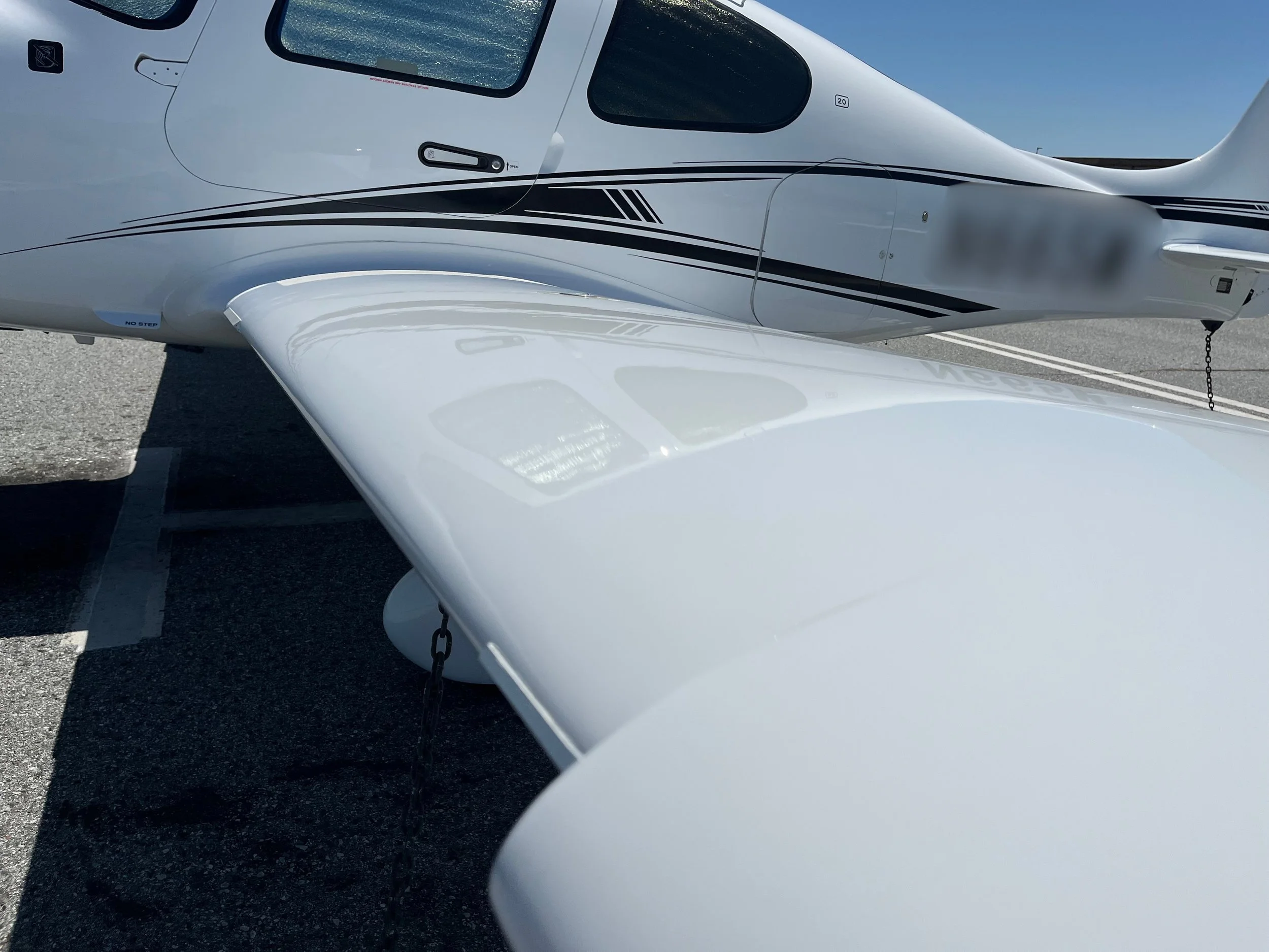 Side view of a white small aircraft or helicopter parked on a tarmac under a clear blue sky.