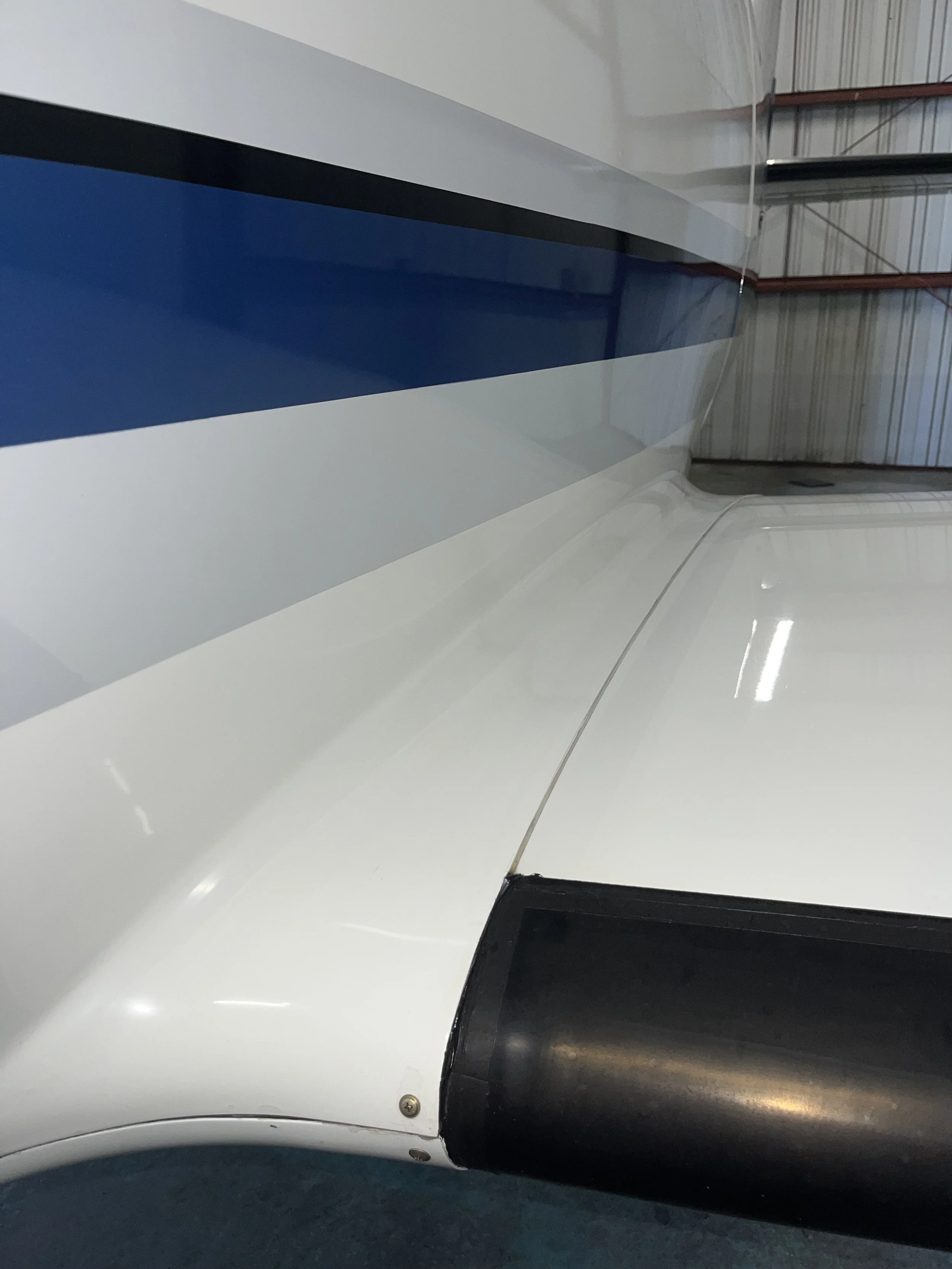 Close-up of the nose of a white airplane with a dark blue stripe and a black radome covering the radar antenna, inside a hangar.