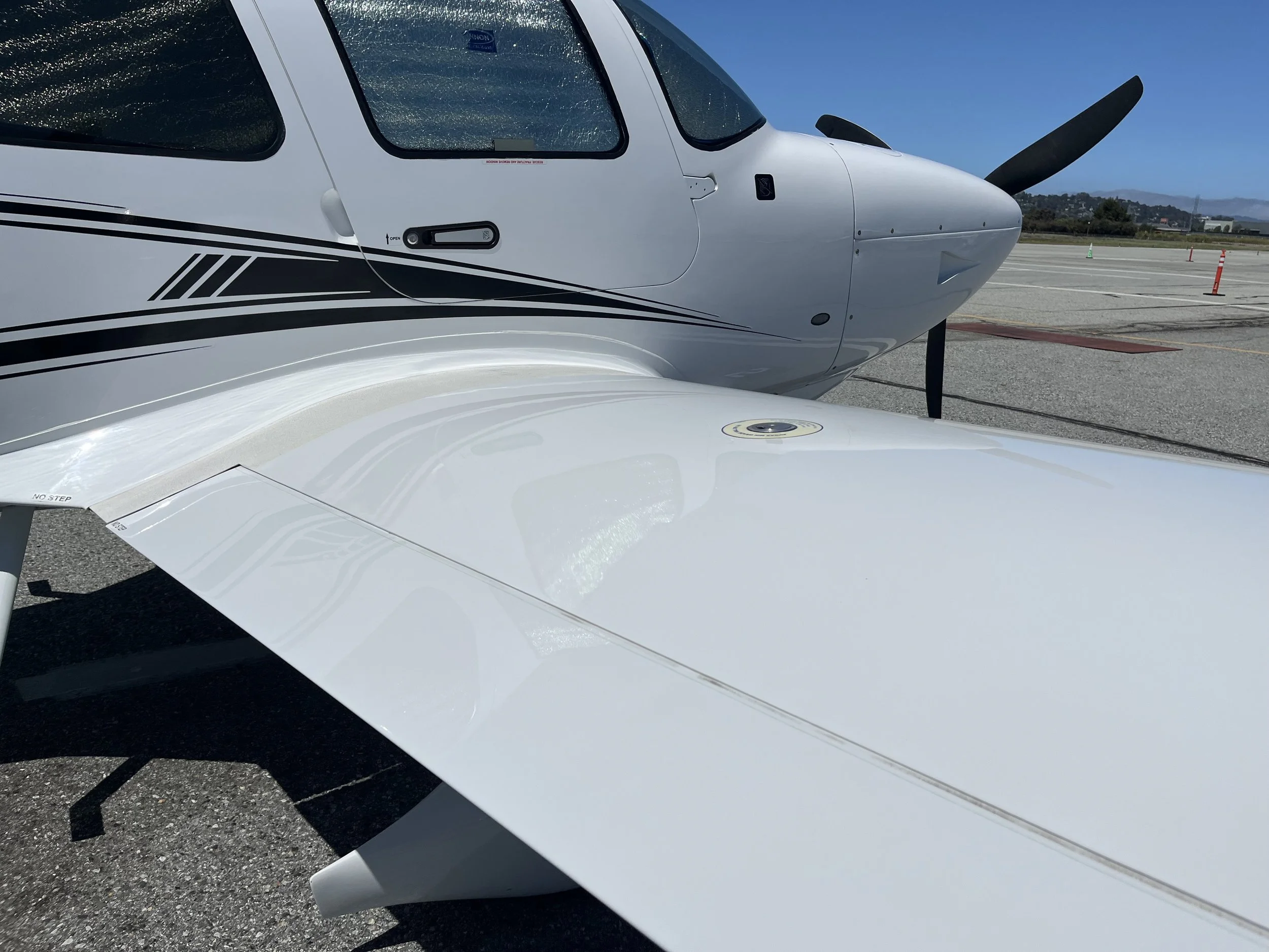 Close-up of the nose and window of a small white private jet aircraft parked on an airfield with mountains in the background.