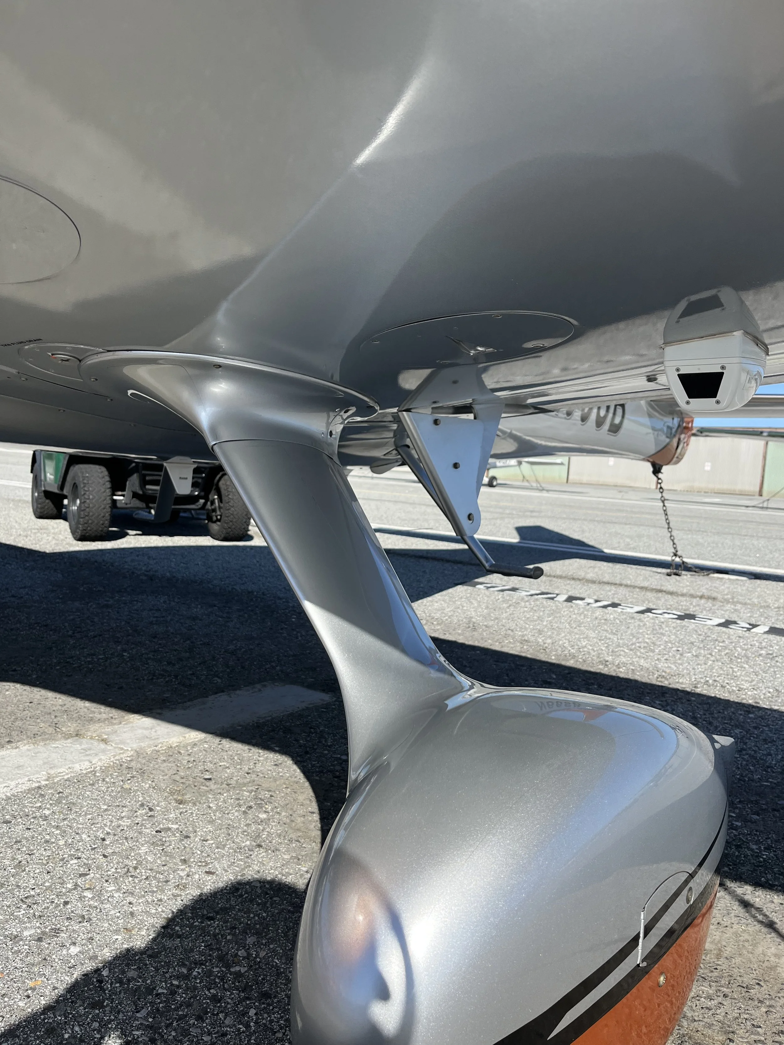 Close-up of a small aircraft's landing gear and wheel resting on tarmac, with a blurred vehicle in the background.