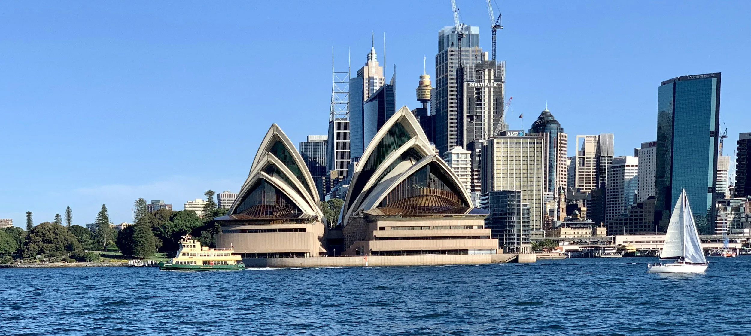 Sydney Opera House with the city skyline in the background and boats on the water.