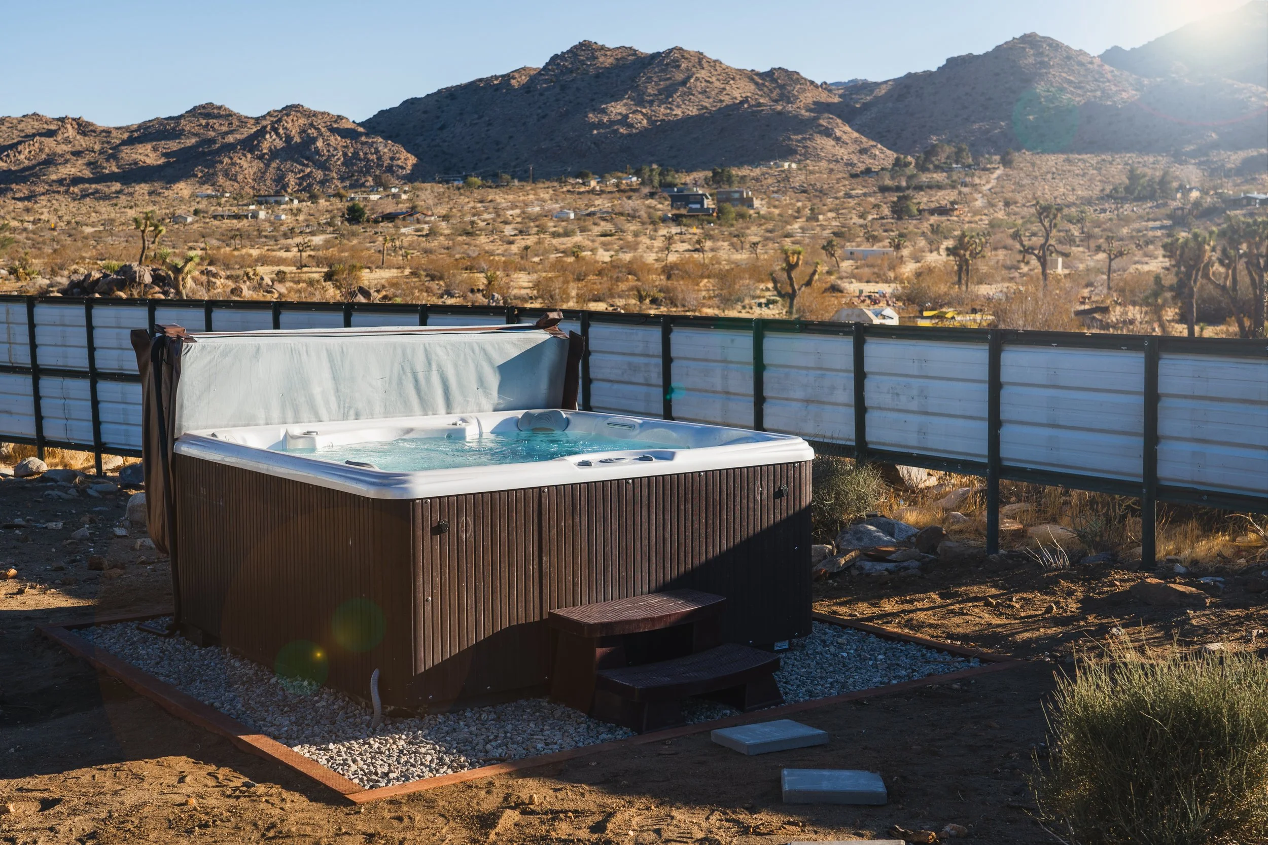 Outdoor hot tub on a gravel base at The Atrium, with rocky desert mountains and Joshua trees behind it