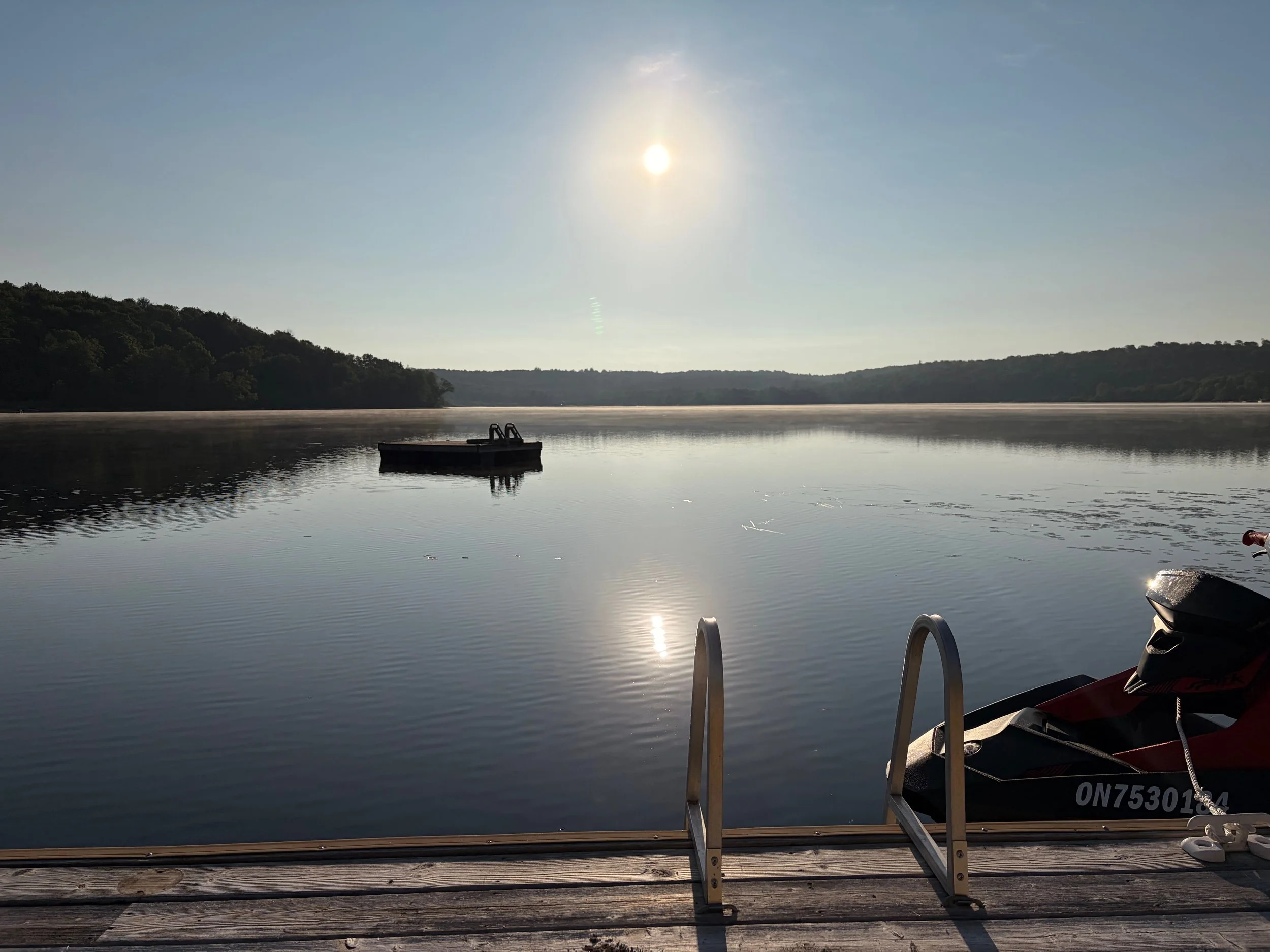 Calm river scene during sunset with a small floating dock in the water and trees in the background. A boat is partially visible on the right side at the dock's edge.