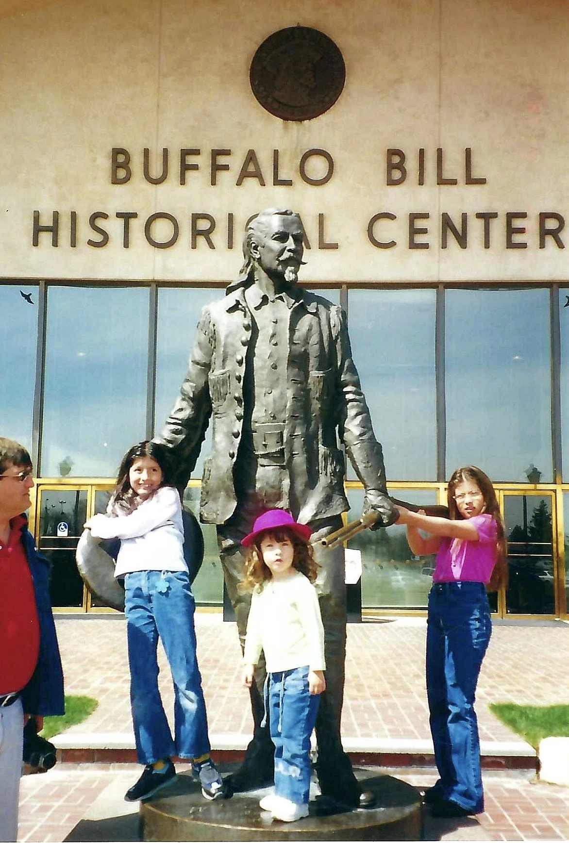 Children posing around a statue of a man in front of the Buffalo Bill Historical Center.
