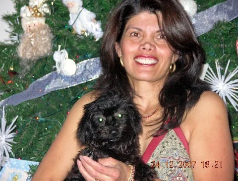 A woman smiling and holding a small black dog in front of a decorated Christmas tree.