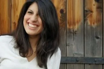 A young woman smiling outdoors in front of a wooden fence.