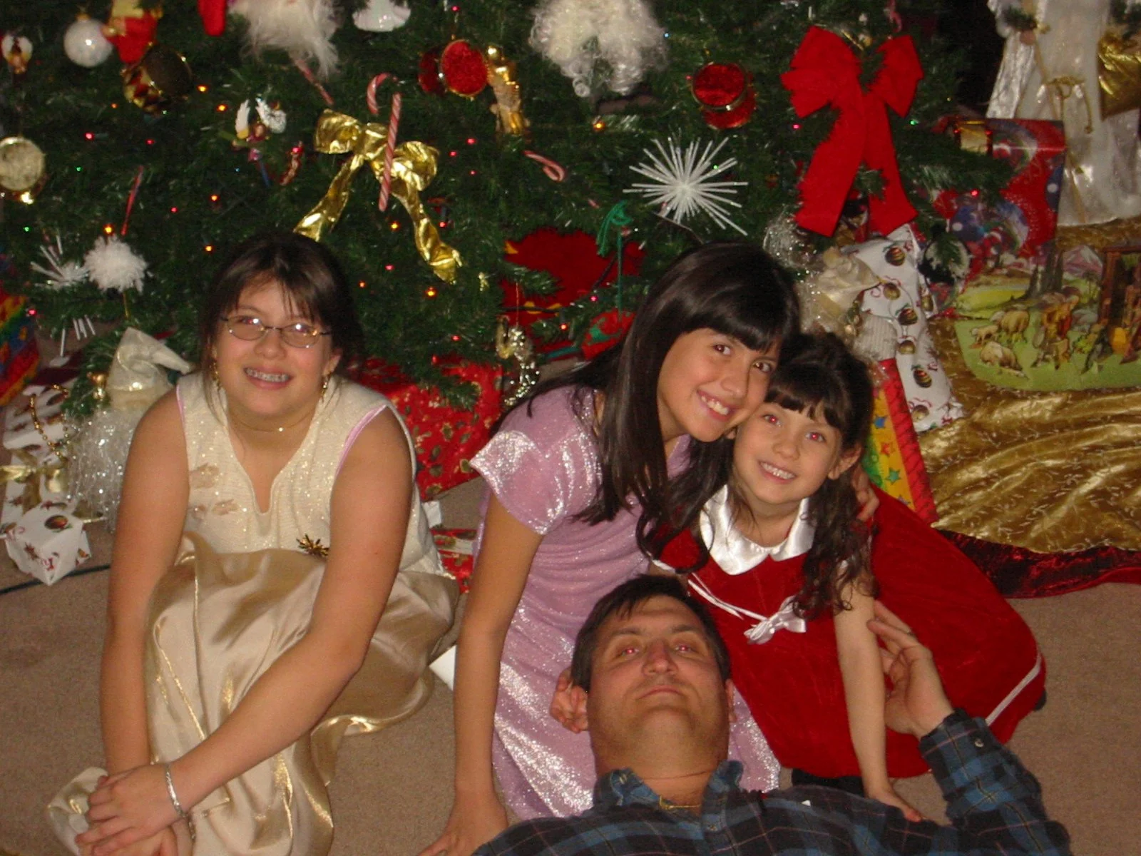 A family of five celebrating Christmas, sitting on the floor in front of a decorated Christmas tree with presents.