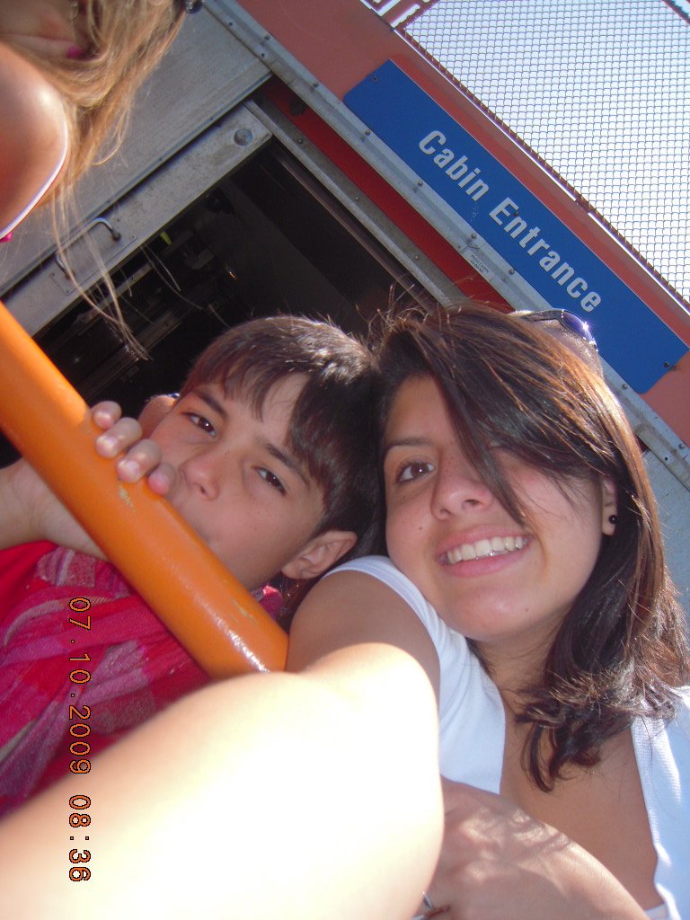 A woman and two children at an amusement park, taking a selfie near a ride with a sign that says 'Cabin Entrance'.