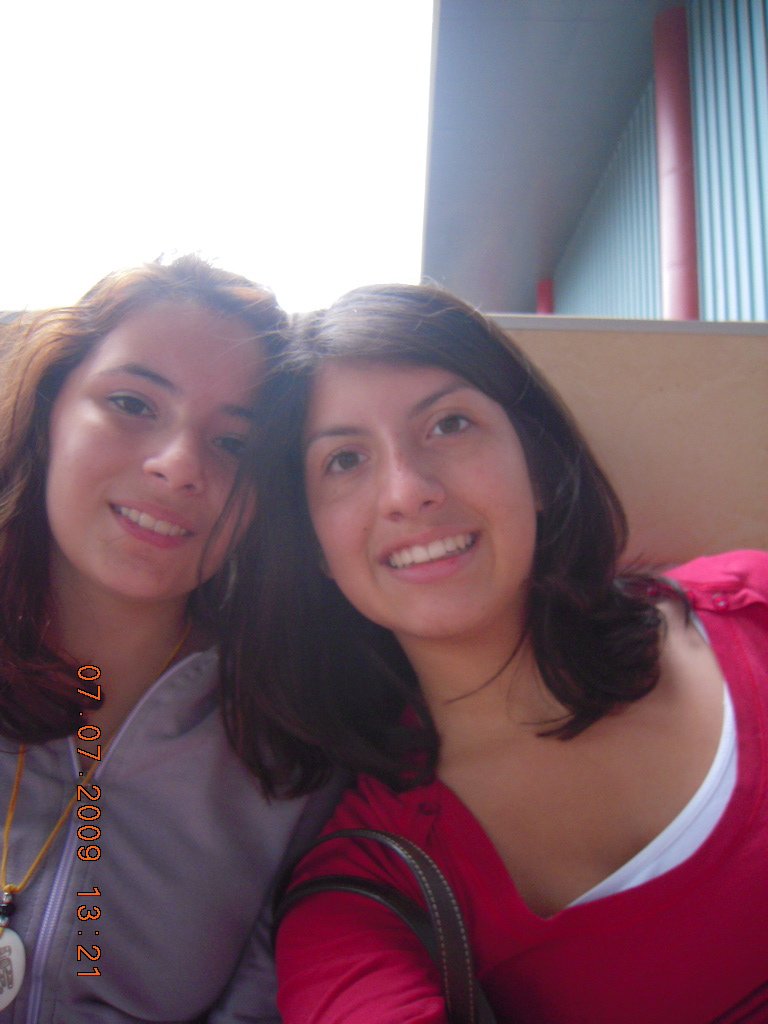 Two young women smiling and taking a selfie together indoors, with a blue and red wall in the background.