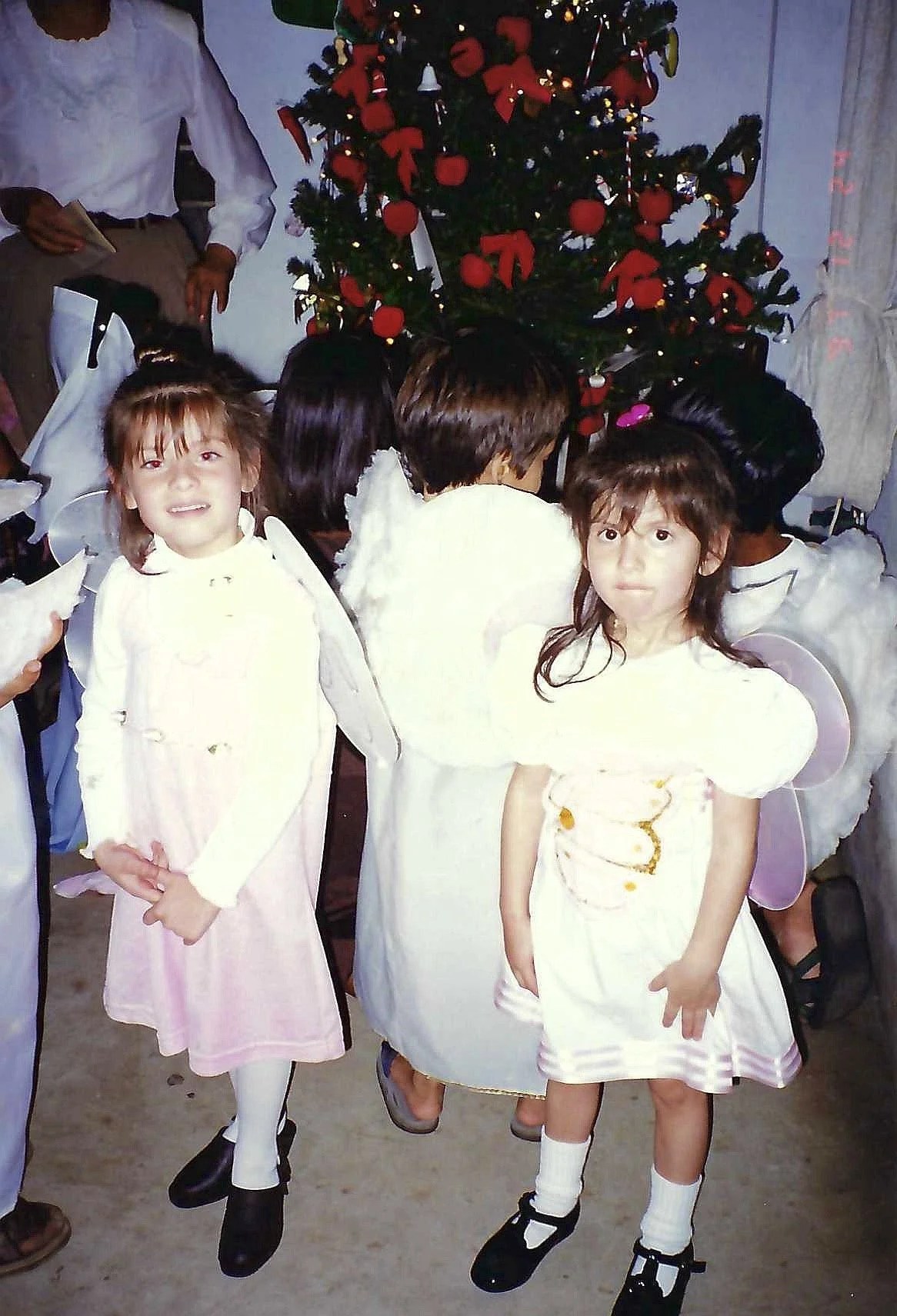 Children dressed as angels standing near a decorated Christmas tree.
