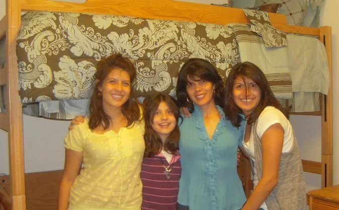 Four women standing close together in front of a bunk bed, smiling at the camera.