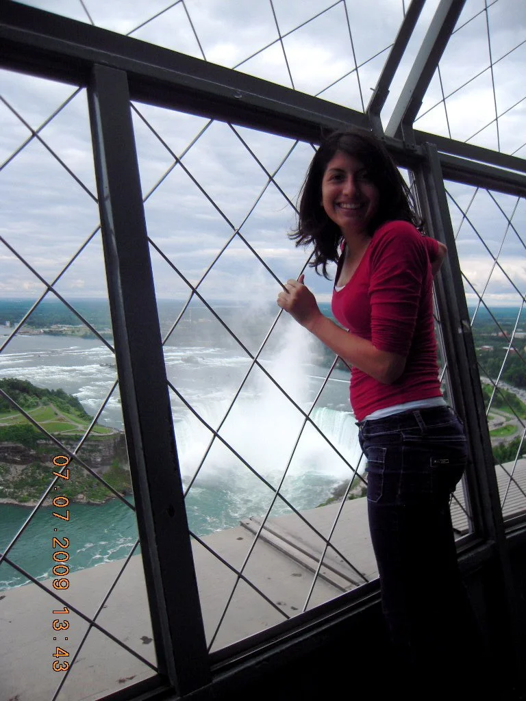 Woman standing inside the observation area of the Eiffel Tower, with Niagara Falls in the background.