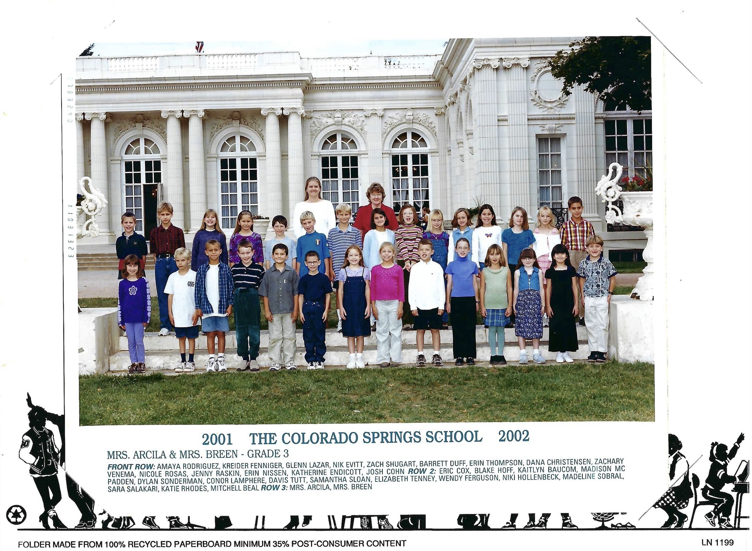 A large group of children and two adults posing outside a white, ornate building with large windows and columns, during daytime.