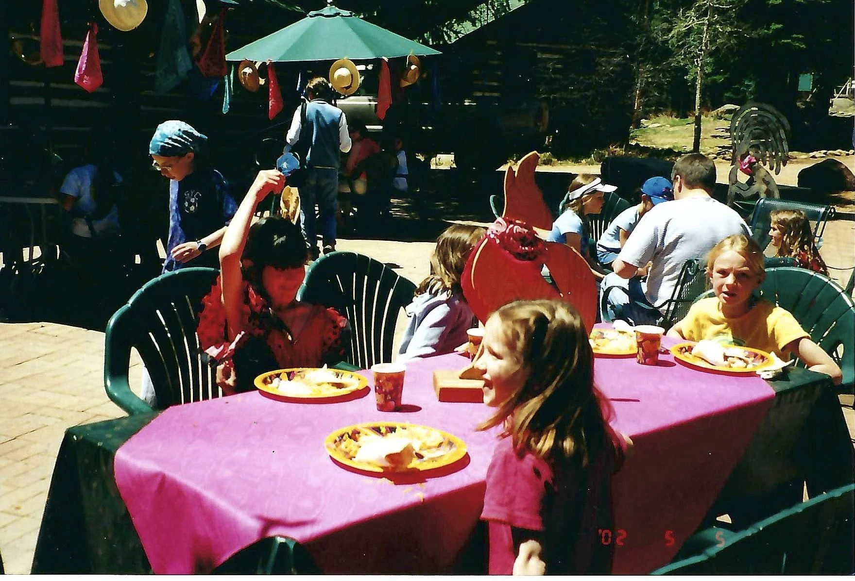 Children and adults at an outdoor birthday party with decorations, food, and a pinata in a backyard.