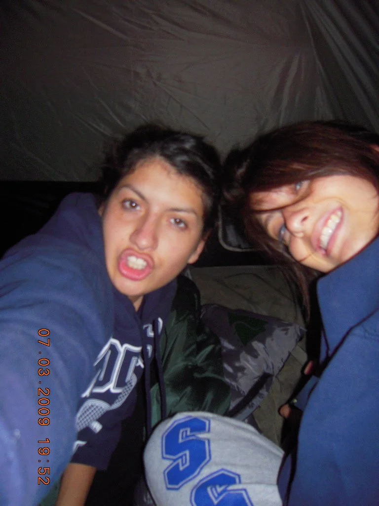 Two young people making silly faces inside a tent, with camping gear visible around them.