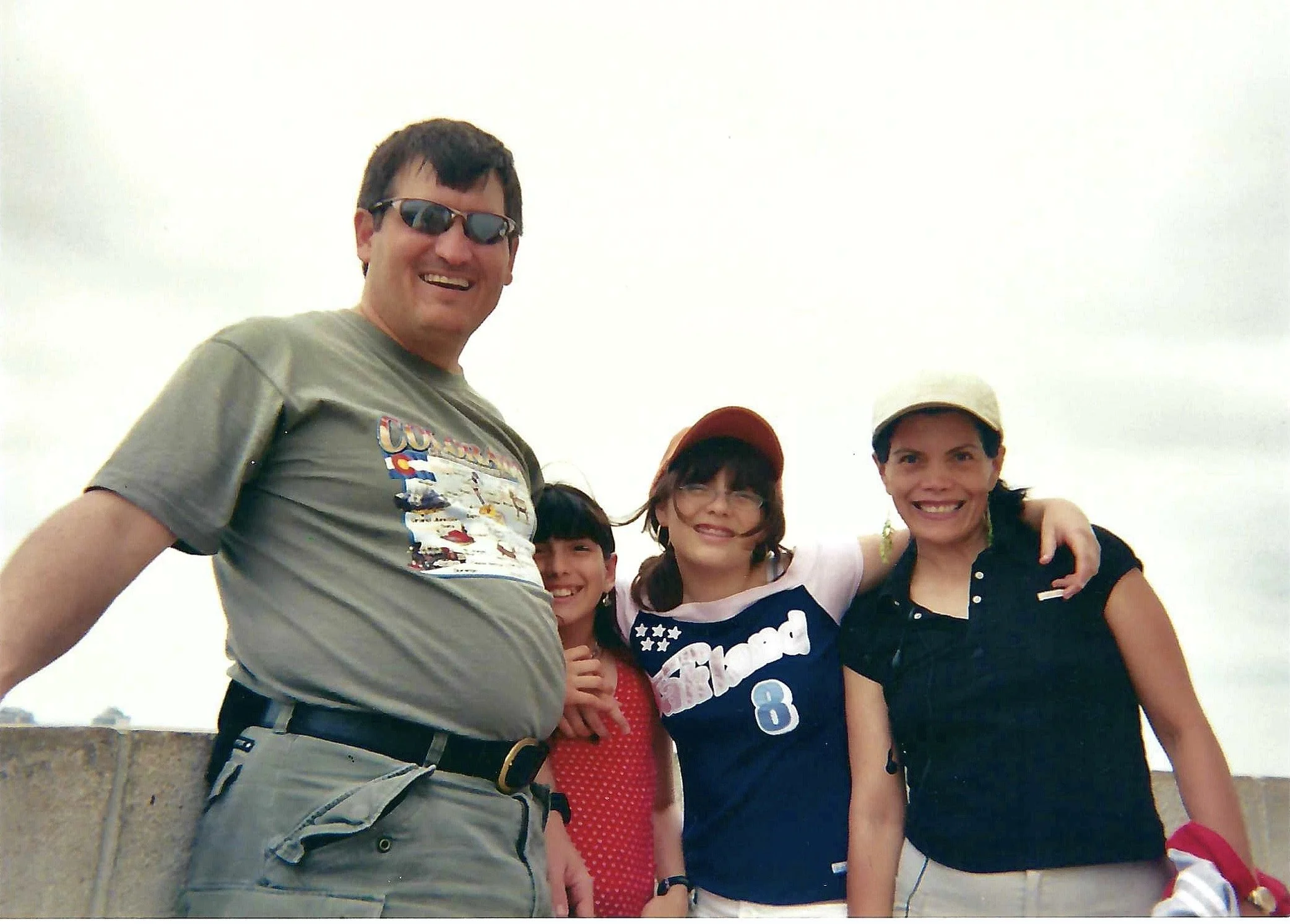 A group of five people smiling and posing together outdoors on a cloudy day.