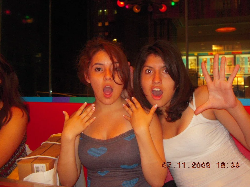 Two women at a restaurant or cafe making surprised or shocked expressions with their mouths open and hands near their faces, sitting at a table.