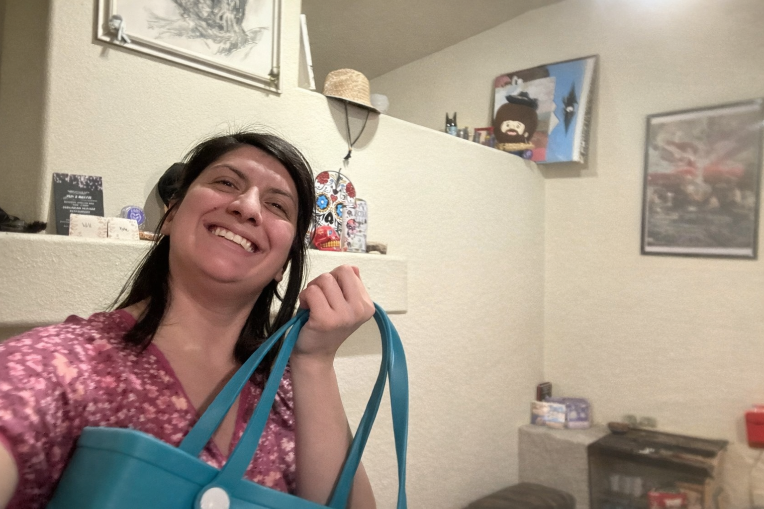 Woman smiling and holding a blue bag in a room with artwork and decorations on the wall.