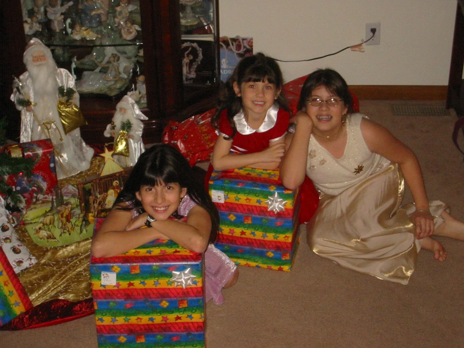 A family with three children celebrating Christmas, surrounded by wrapped gifts and holiday decorations, including a Christmas tree and Santa figurines.