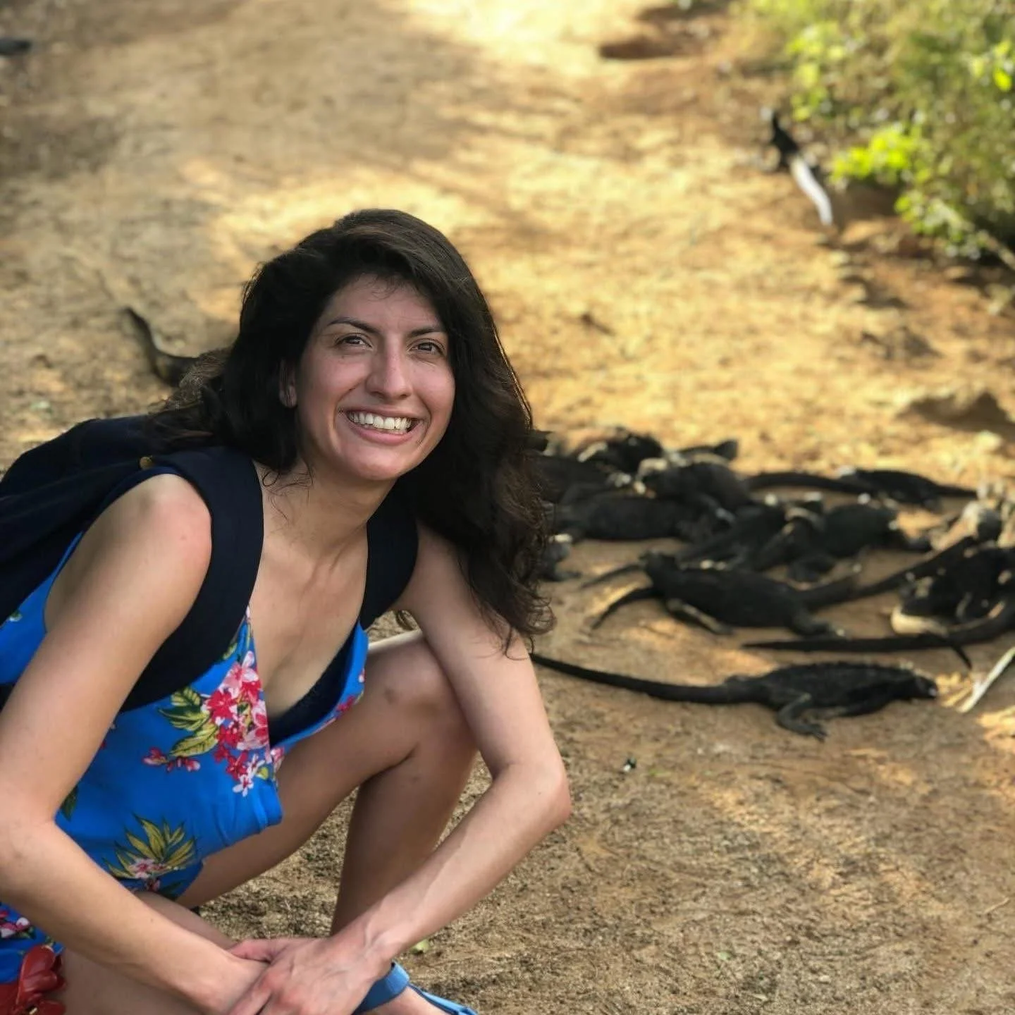 A woman crouching with a group of black caiman crocodiles on a sandy riverbank.