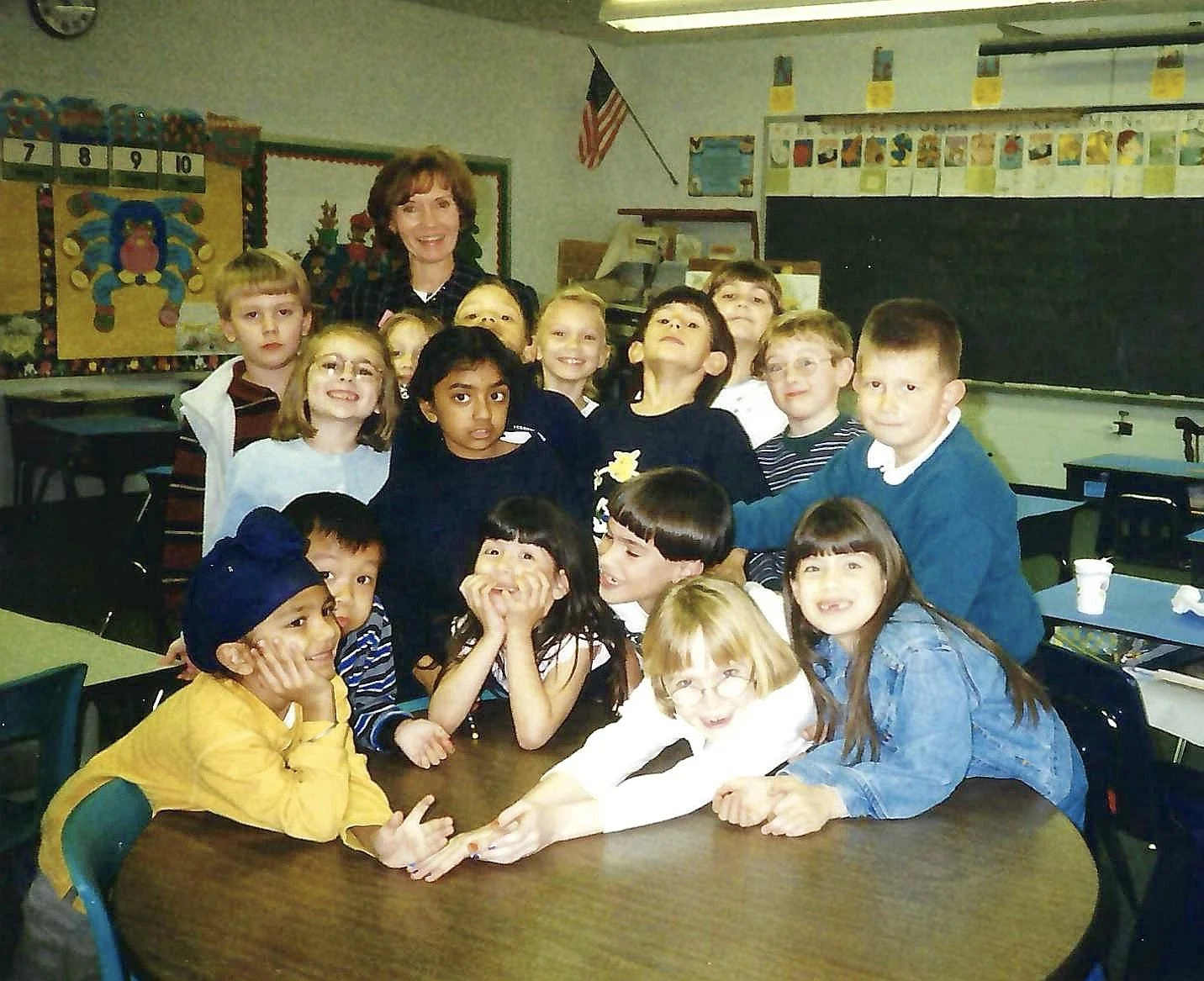 A group of children and a teacher posing together in a classroom.