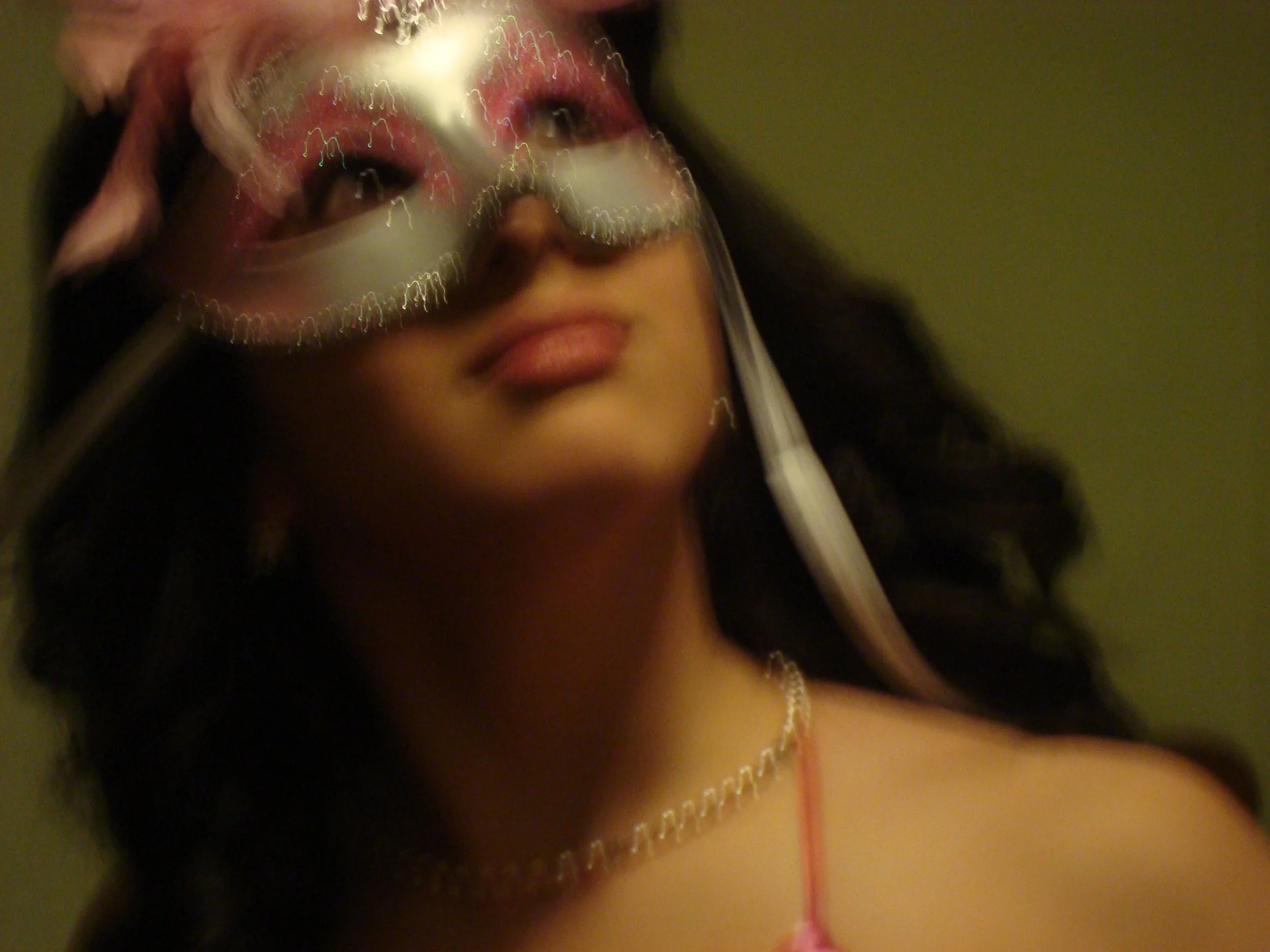 Close-up of a woman wearing a decorative eye mask with red, white, and silver details, and a layered pearl necklace.