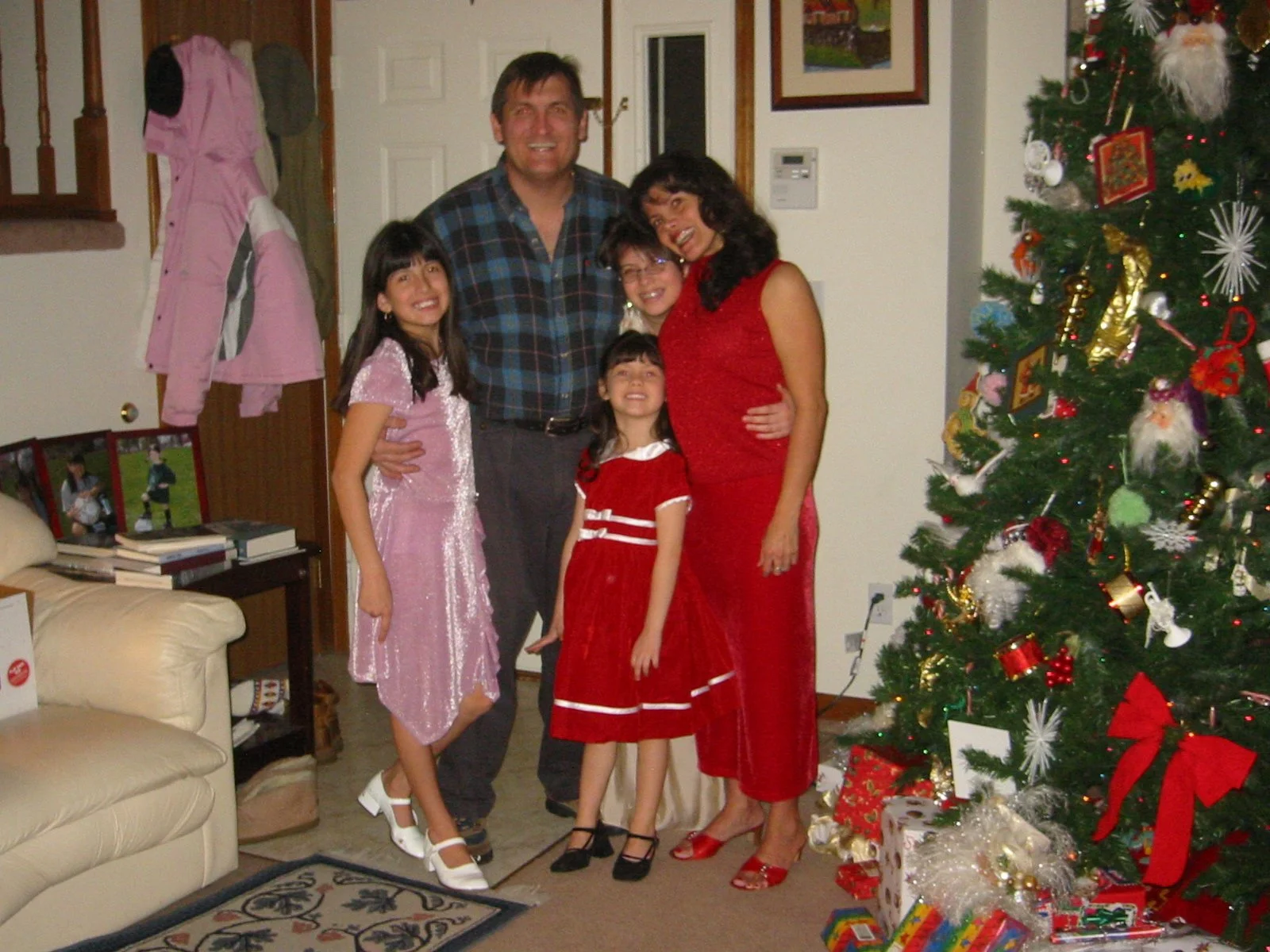 A family gathered around a Christmas tree decorated with ornaments and presents underneath, smiling for the camera in a living room.
