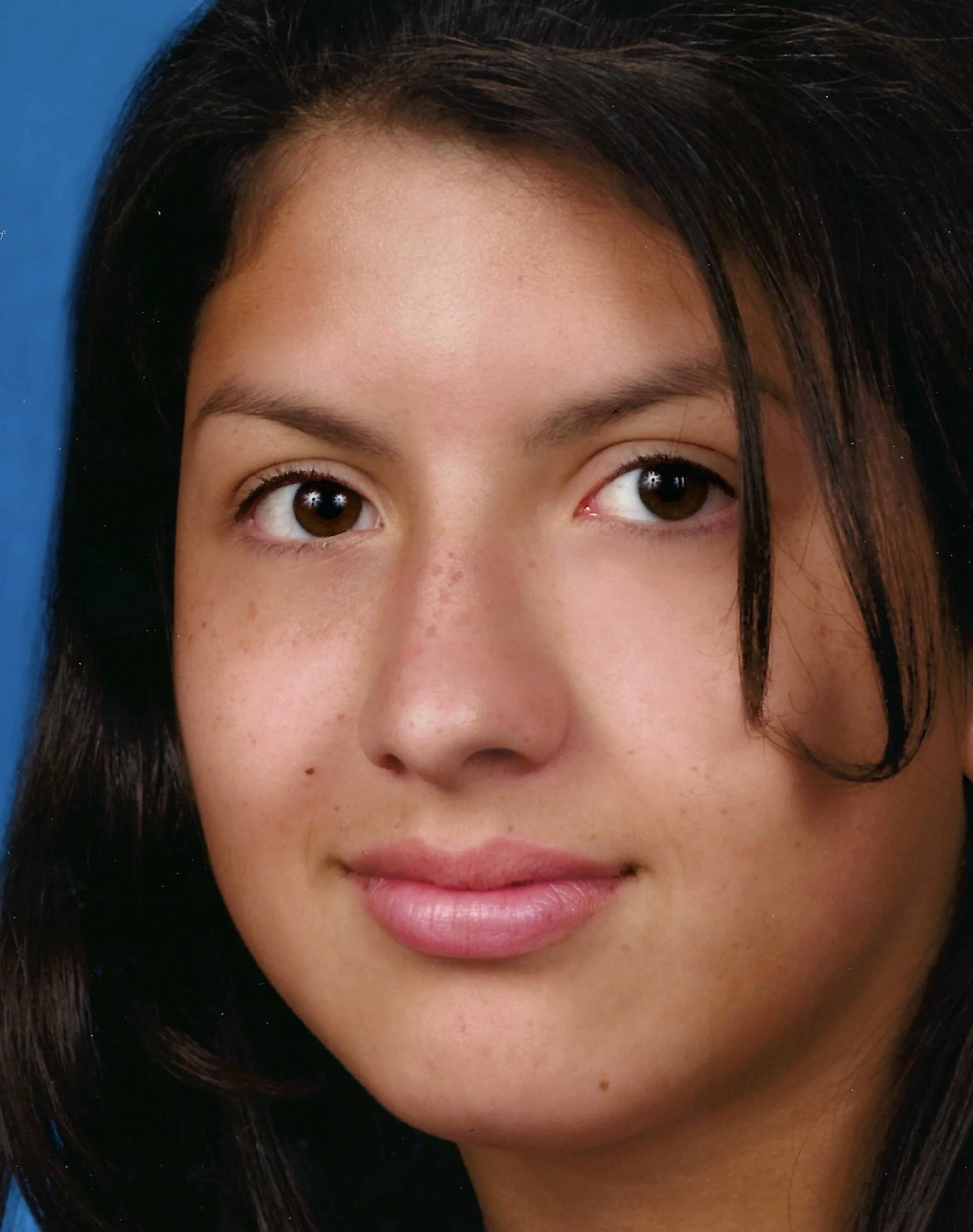 Close-up of a woman's face showing brown eyes, full lips, and dark hair against a blue background.