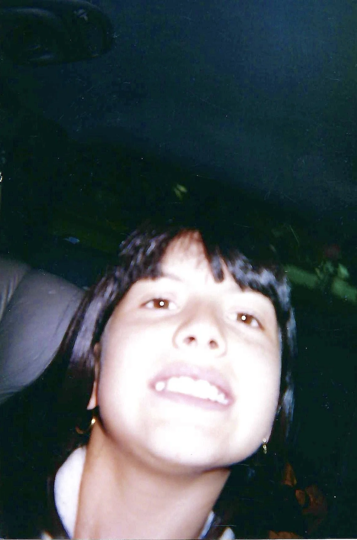 A close-up selfie of a young person with black hair, partially lying on a seat, with a dark background visible at the top.