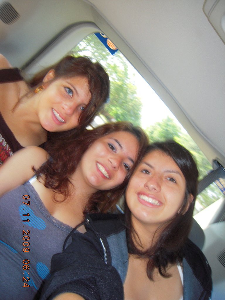 Three women taking a selfie inside a vehicle on a sunny day, with trees visible outside the window.