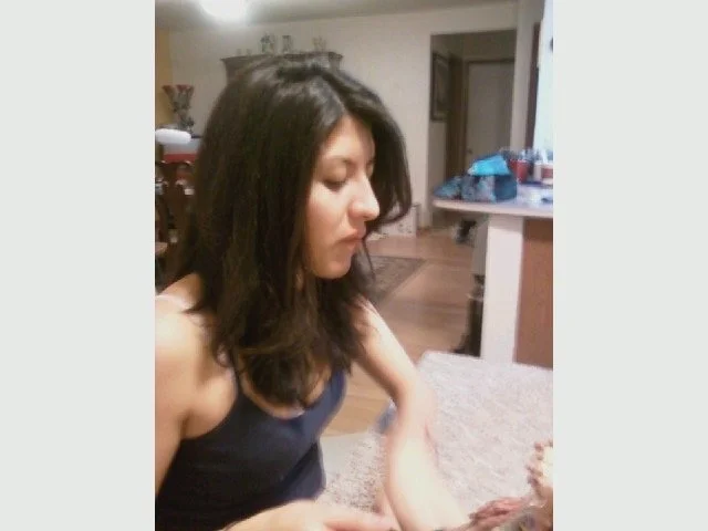 Side profile of a woman with dark hair sitting in a home environment.