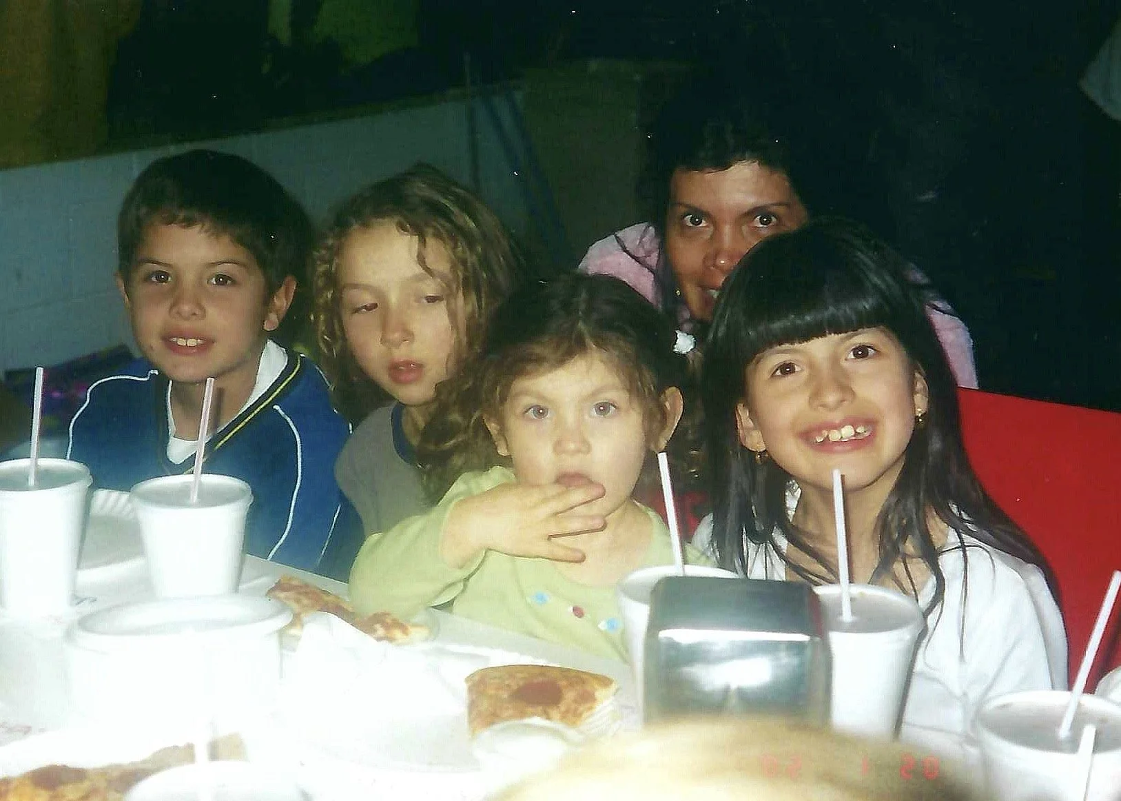 Children sitting at a table with drinks and pizza, posing for a photo.
