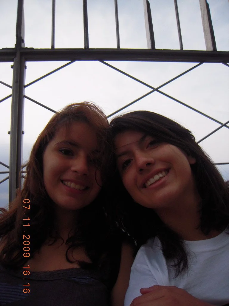 Two women smiling, under a metal and glass structure.