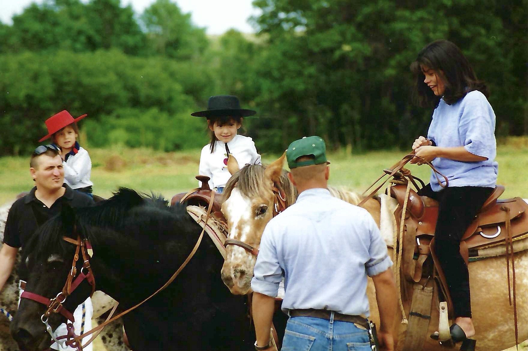 People riding horses outdoors with trees in the background