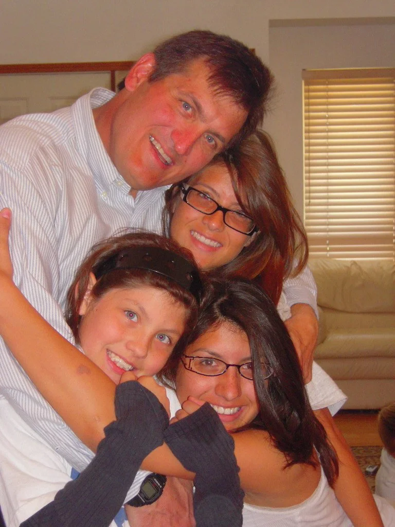 A family of four smiling and hugging in a home interior.