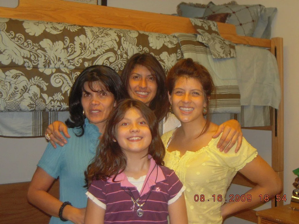 Four women and a girl smiling in a bedroom, with bunk beds and floral bedding in the background.