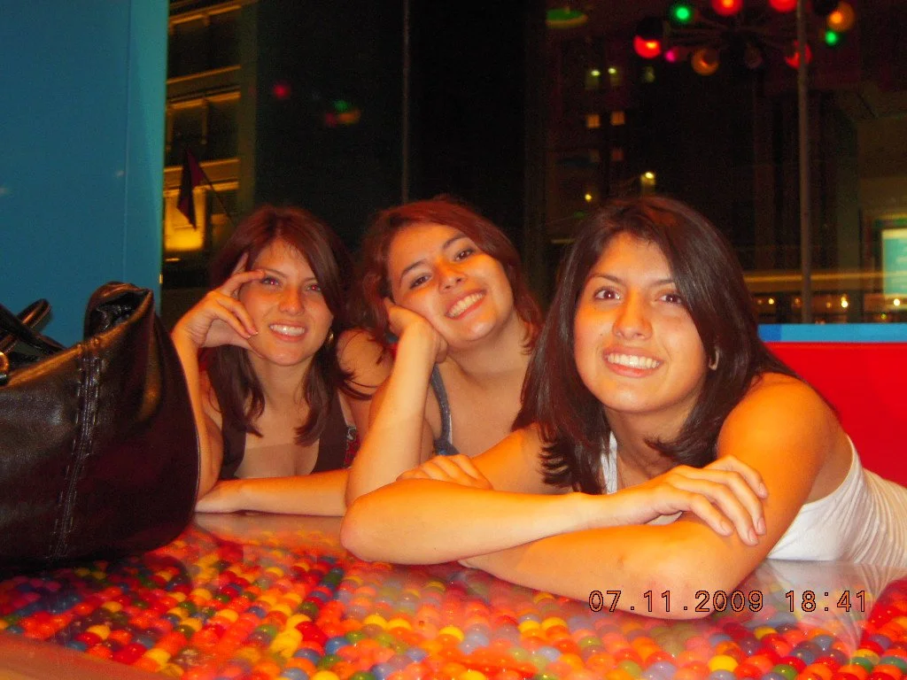 Three women sitting at a colorful table, smiling at the camera.