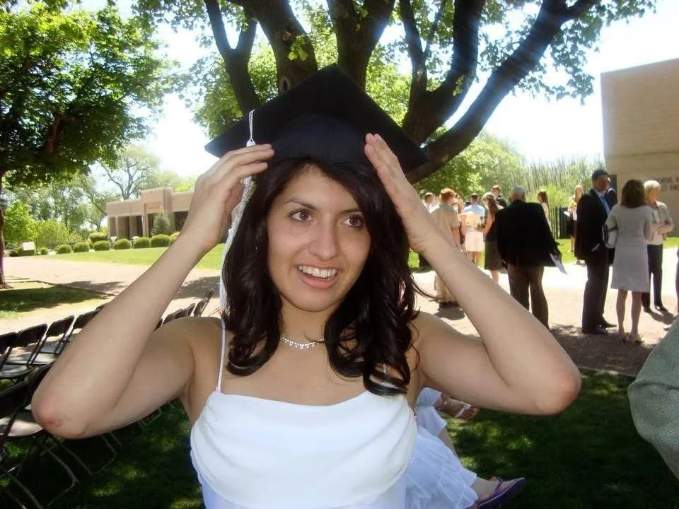 Young woman in a white dress adjusting a graduation cap outdoors at a graduation ceremony.