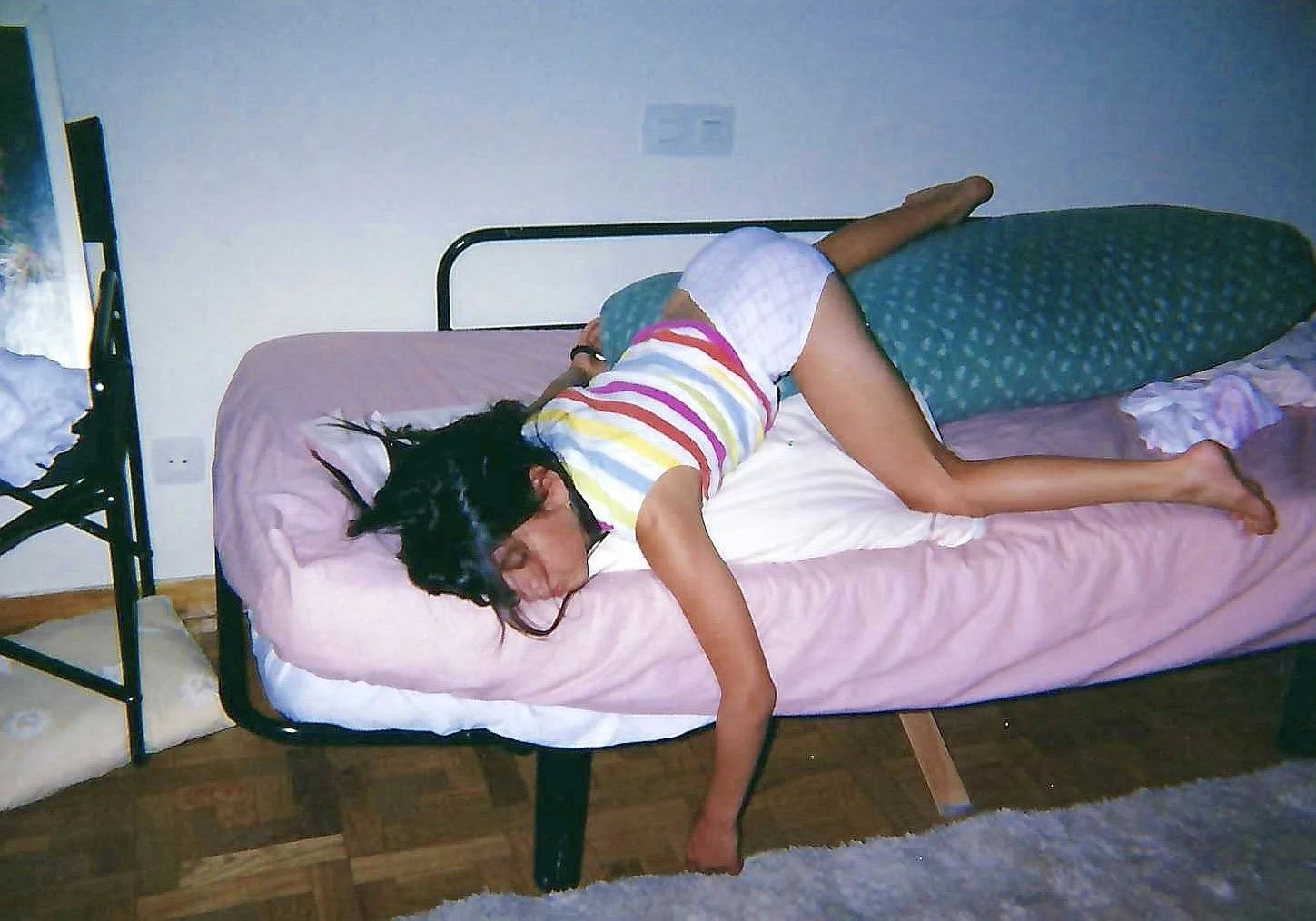Child sleeping on a bed with pink sheets, wearing a striped shirt and shorts, lying on her side with hair spread out on the pillow.