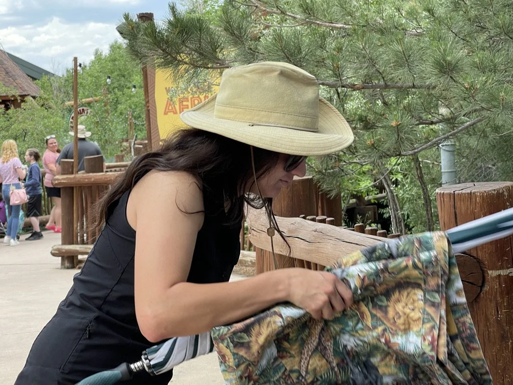 Woman wearing a wide-brimmed hat and sunglasses, looking at a towel or cloth with a tropical print.