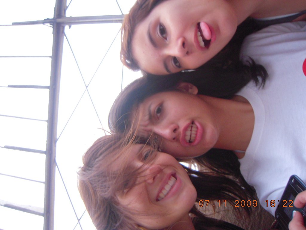 Three young women making silly faces at the camera, with a metal structure and blue sky in the background.