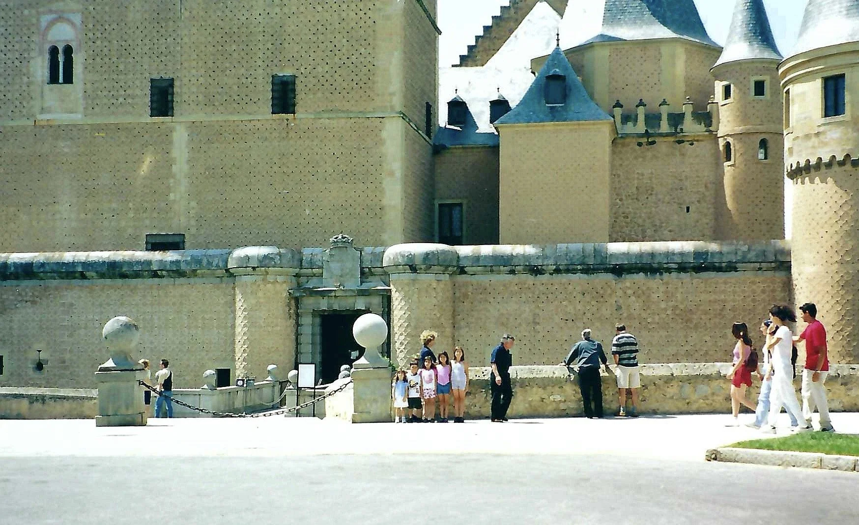 People walking in front of a castle with beige stone walls and blue cone-shaped roofs on the towers.