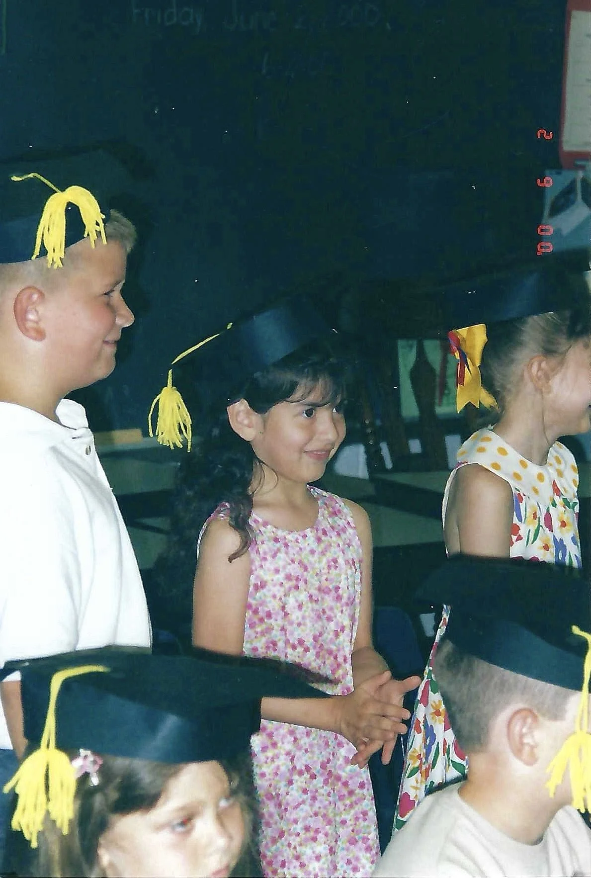 Children at a graduation ceremony, some wearing black caps with yellow tassels, standing in a line and facing forward.