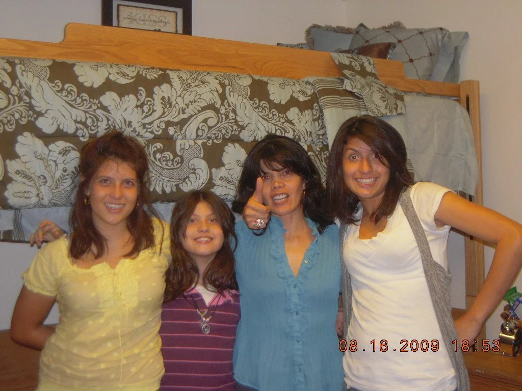 Four women and a girl standing together in a bedroom, smiling at the camera. There is a bed with an ornate floral sheet and pillows in the background. The photo is dated August 16, 2009, at 6:53 PM.