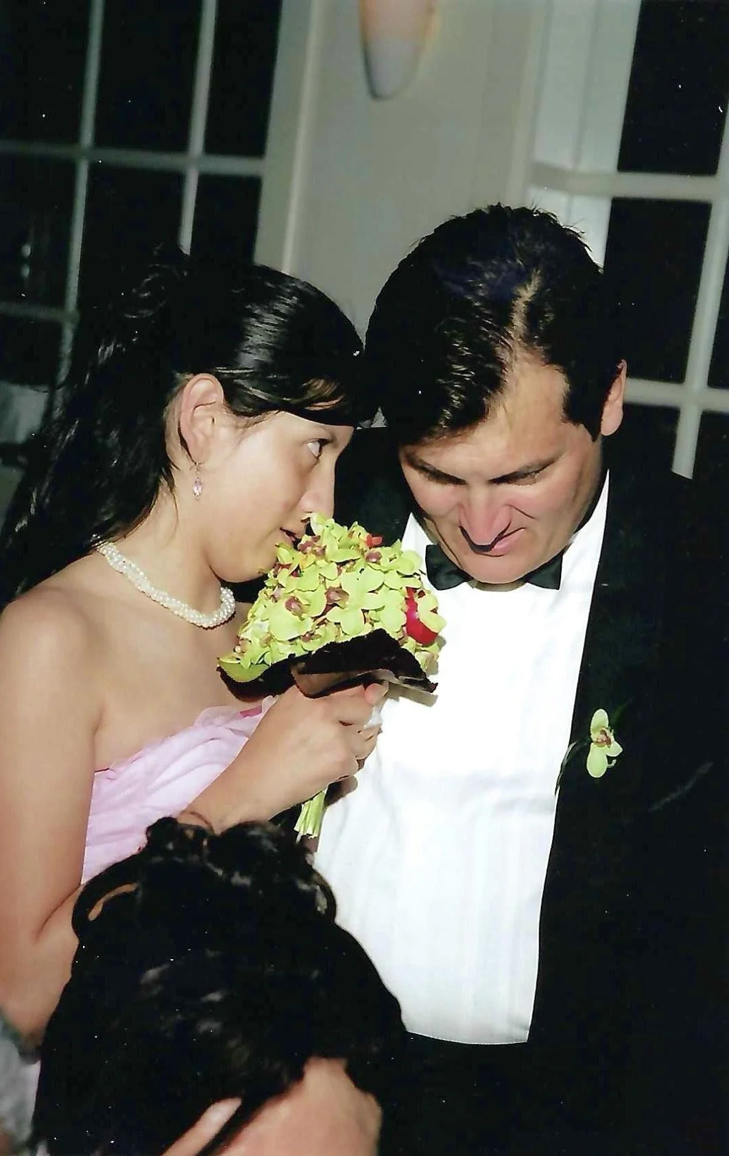 A bride and groom in formal attire holding a bouquet, closely leaning their foreheads together during wedding celebration.